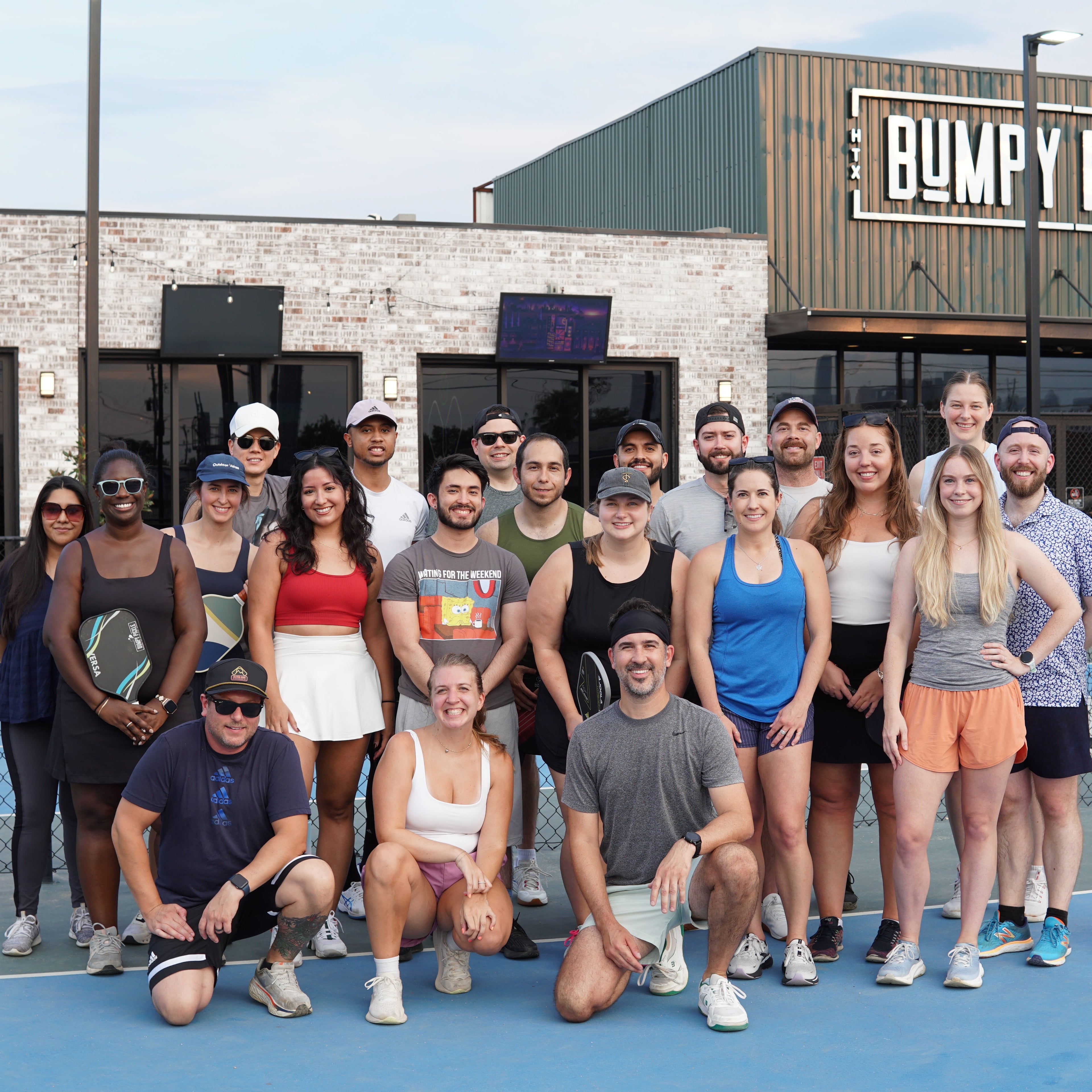 Group of Silly Pickles players posing on a pickleball court in front of a building with &