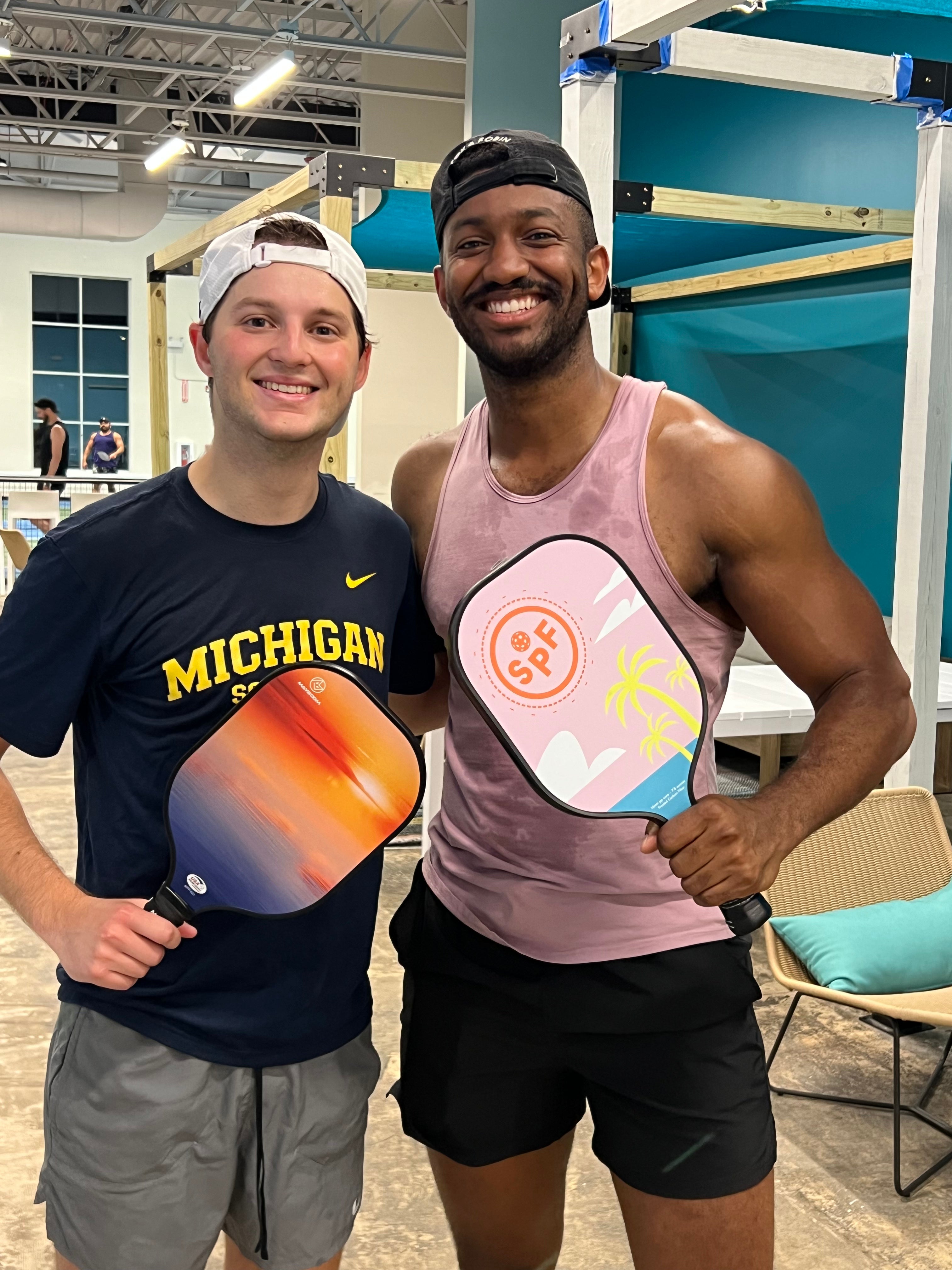 Two men holding pickleball paddles in an indoor setting