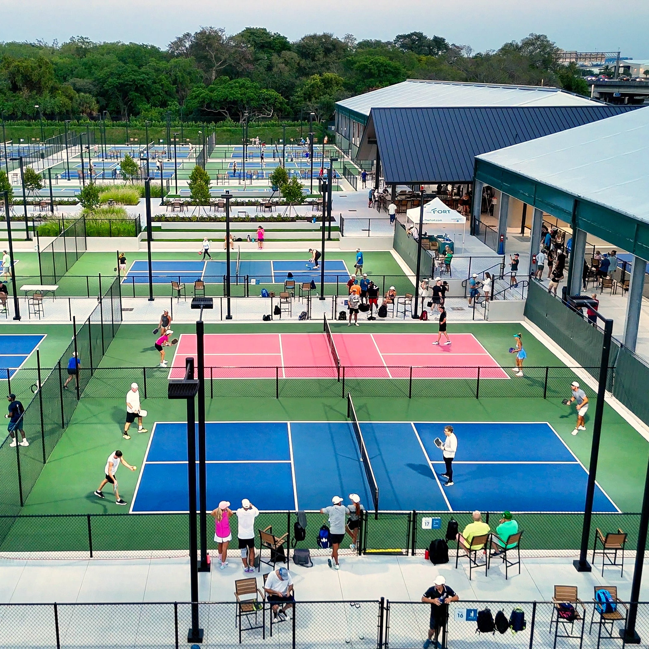 Outdoor pickleball courts with players and spectators in a park setting.