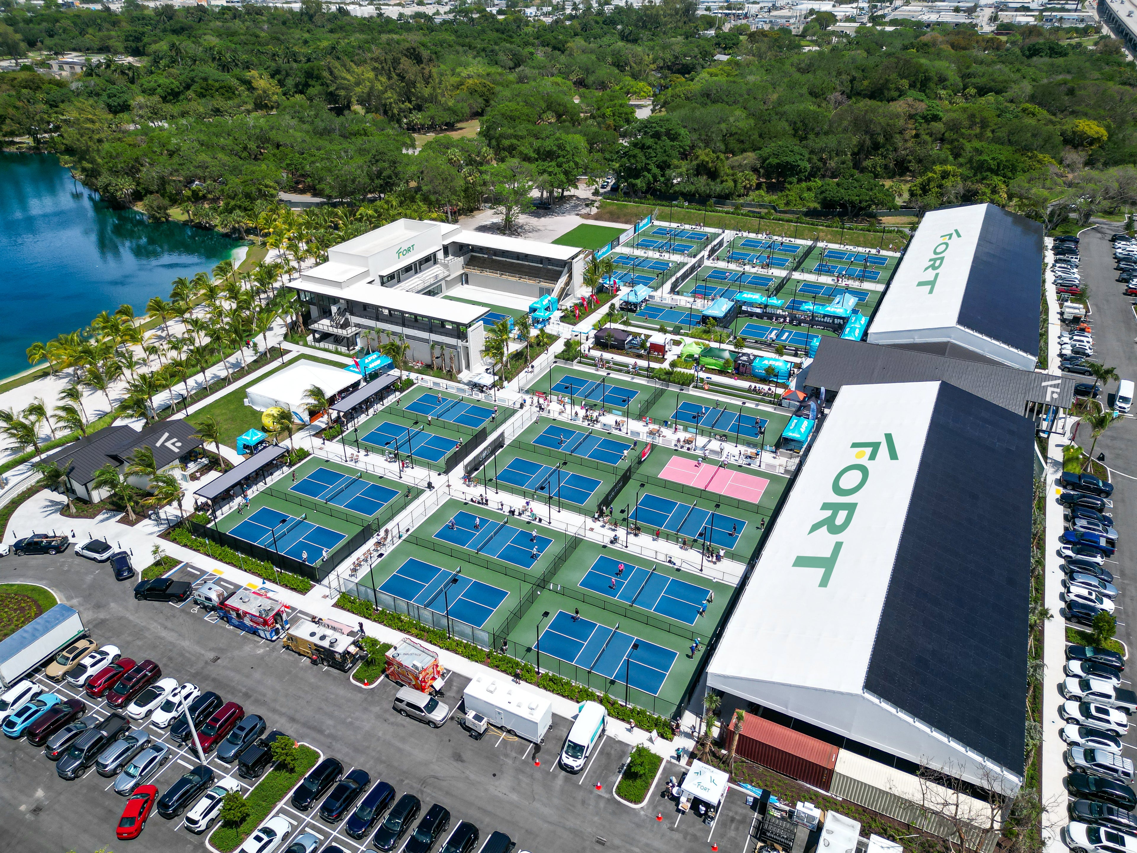 Aerial view of a pickleball complex with multiple courts and surrounding parking lot.