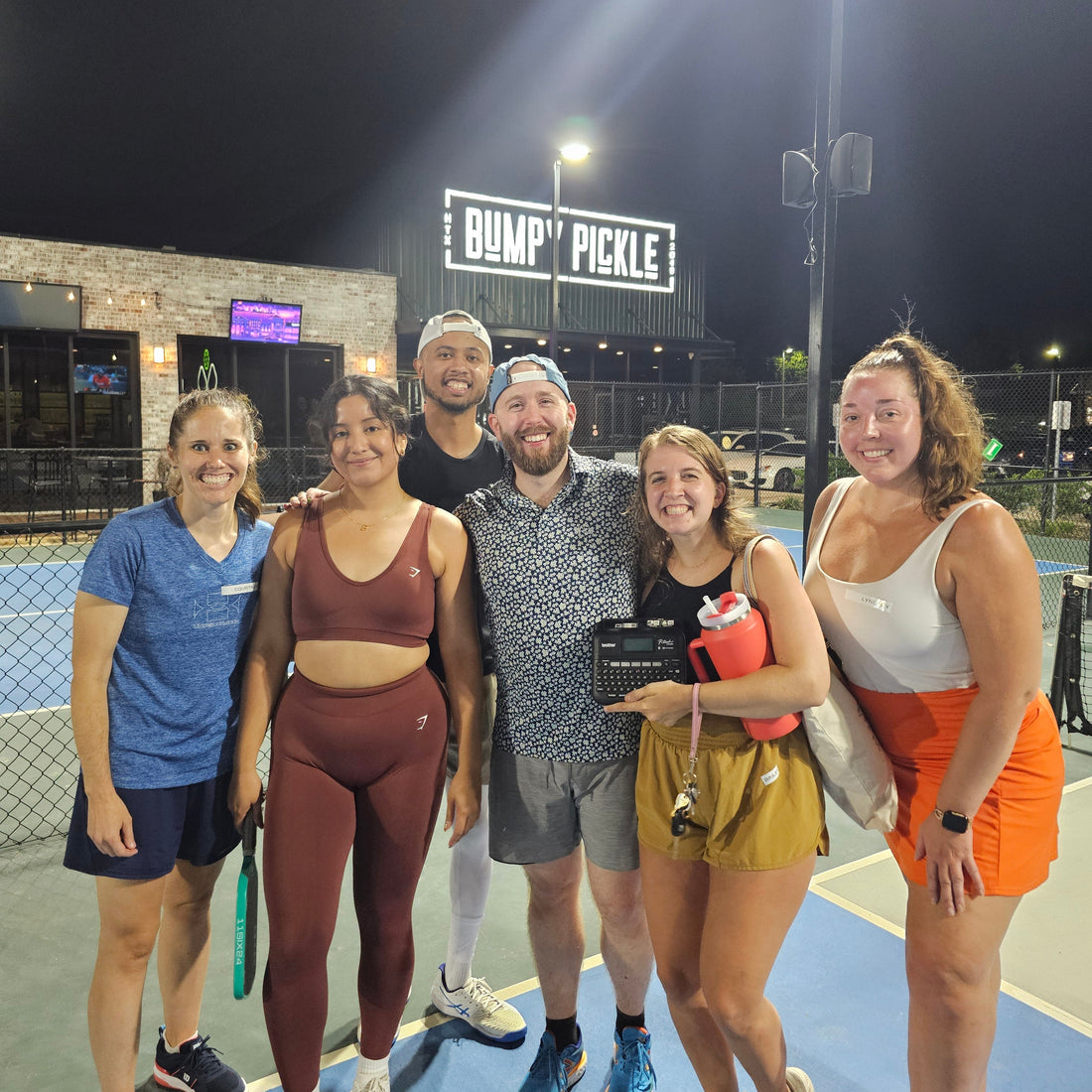 Group of Silly Pickles players posing together on a pickleball court at night.