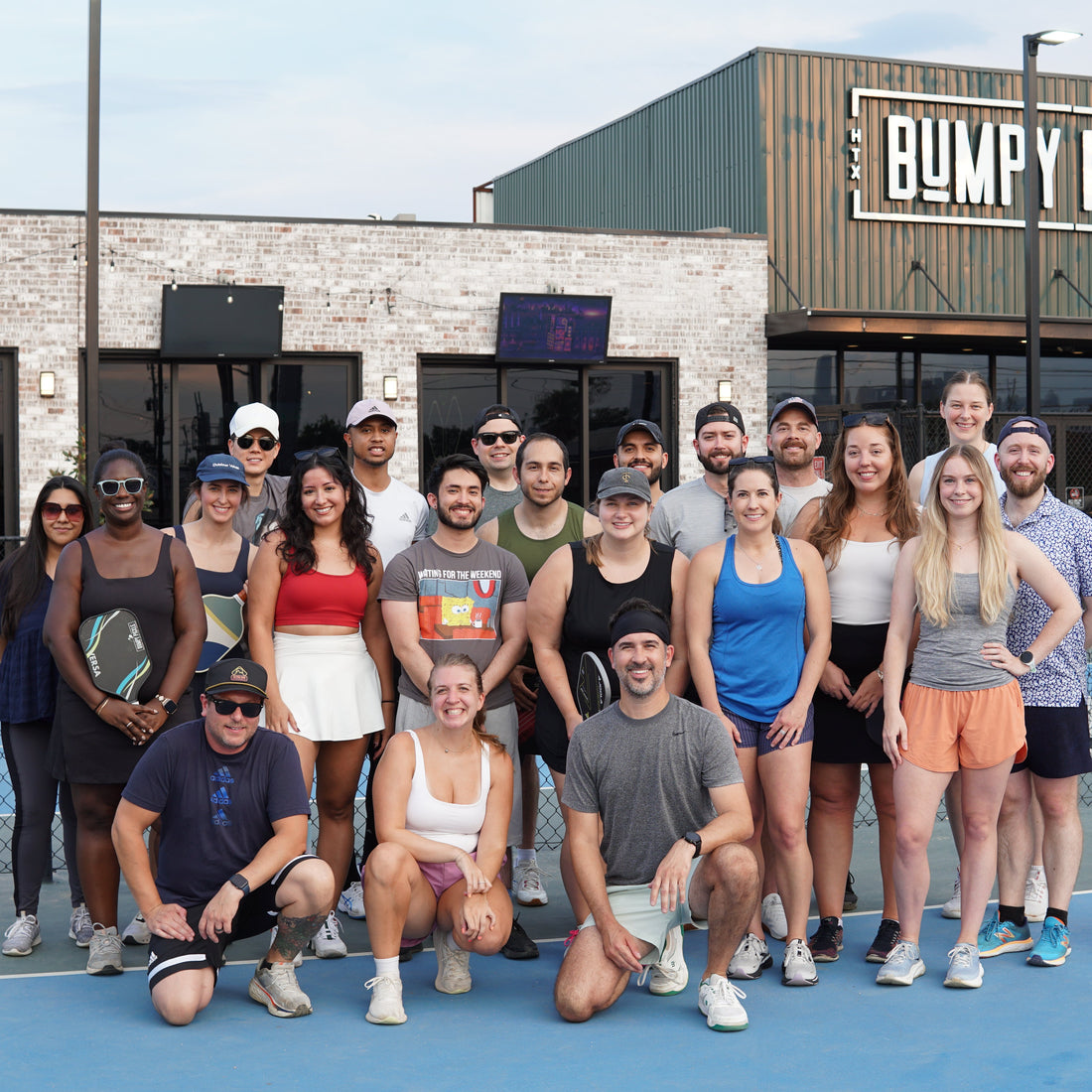 Group of Silly Pickles players posing on a pickleball court in front of a building with &
