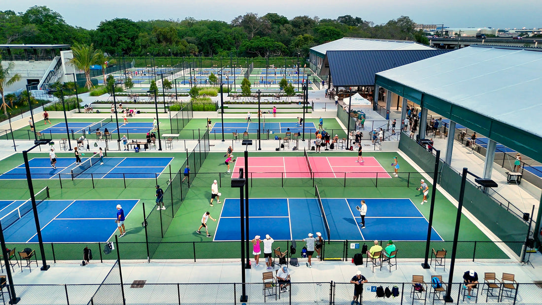 Outdoor pickleball courts with players and spectators in a park setting.