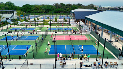 Outdoor pickleball courts with players and spectators in a park setting.
